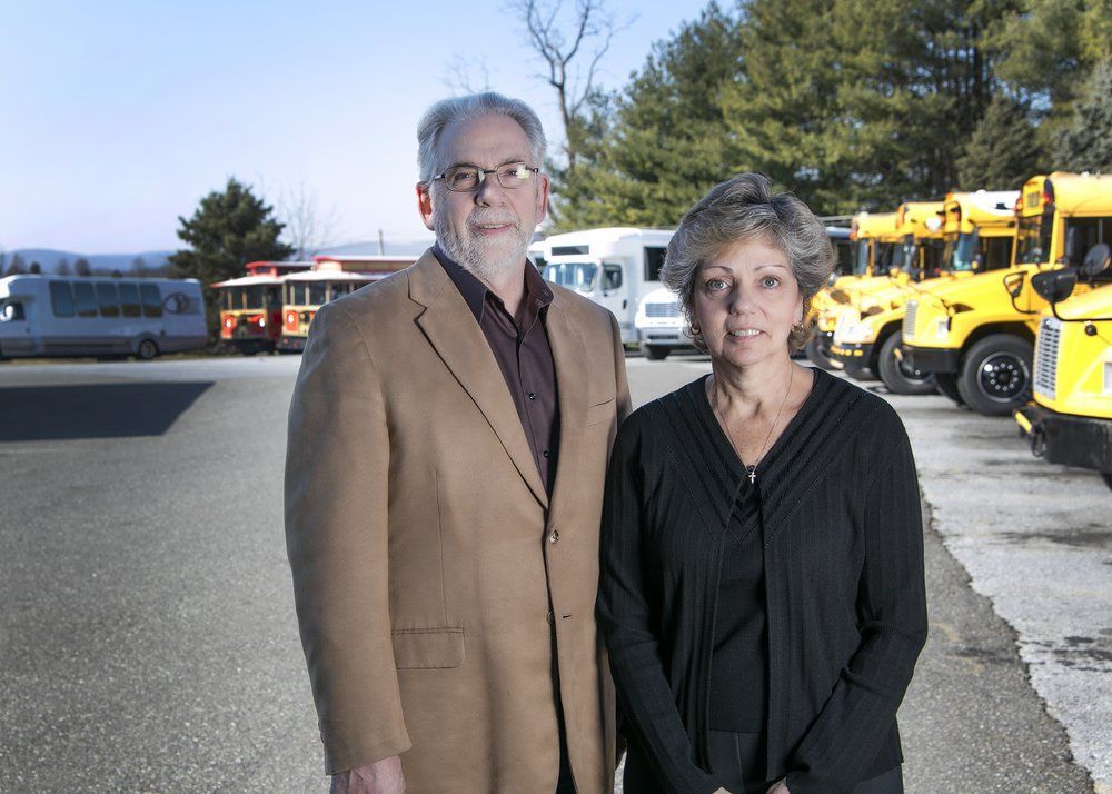 Two people standing outdoors near buses and yellow trucks on a sunny day