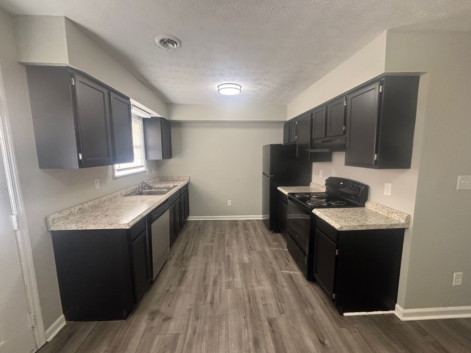 A kitchen with black cabinets , granite counter tops , a stove , refrigerator and sink.