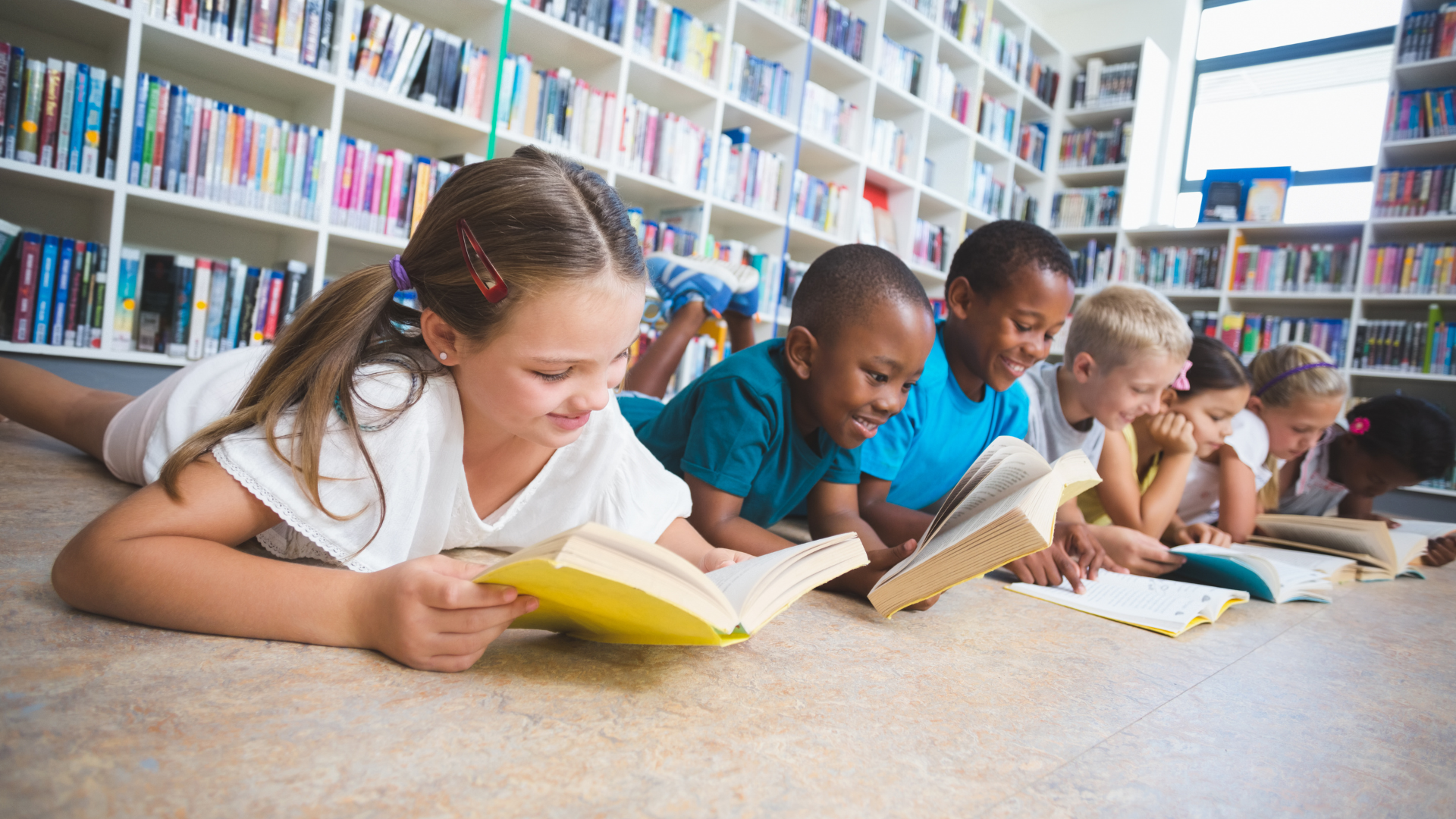 Children lying on the floor reading books in a library.