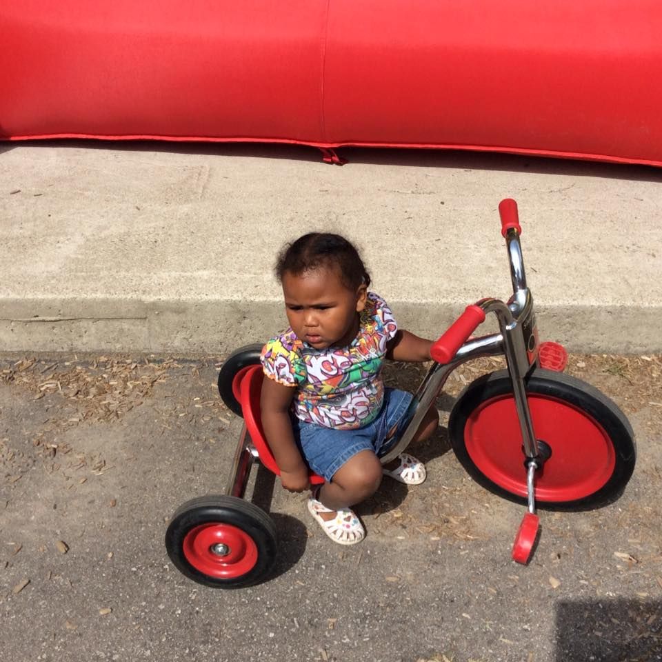 A little girl is sitting on a red tricycle