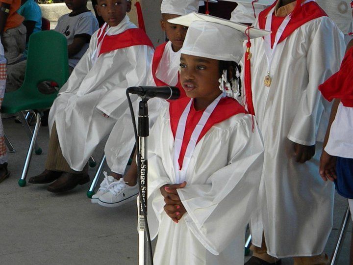 A young girl in a graduation cap and gown stands in front of a microphone