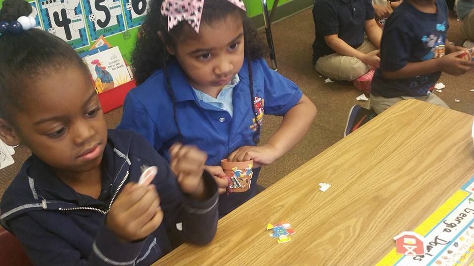 Two young girls are sitting at a table in a classroom eating ice cream