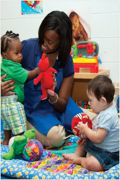 A woman is sitting on the floor with two babies playing with toys