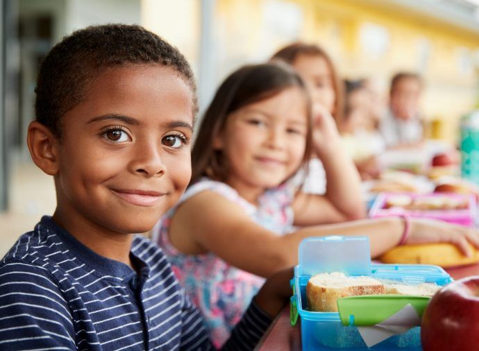 Children smiling at a school lunch table with colorful lunch containers