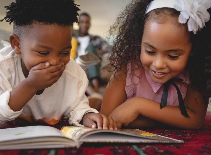 Two children smiling and reading a book together at a table