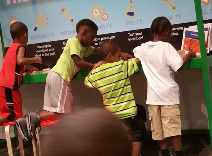 Children leaning on a green counter at an indoor science exhibit