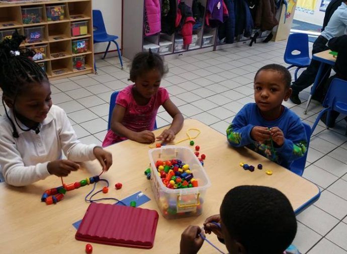 Children playing with colorful beads at a classroom table with a clear bin of supplies.