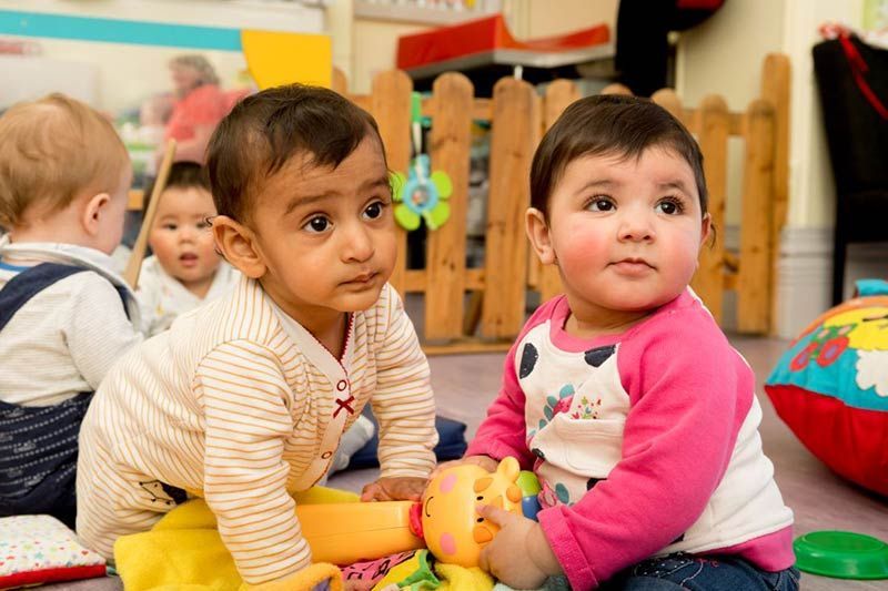 Two babies are sitting on the floor playing with toys.