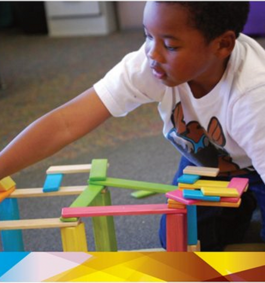 Child building a colorful block structure on the floor, reaching toward the pieces