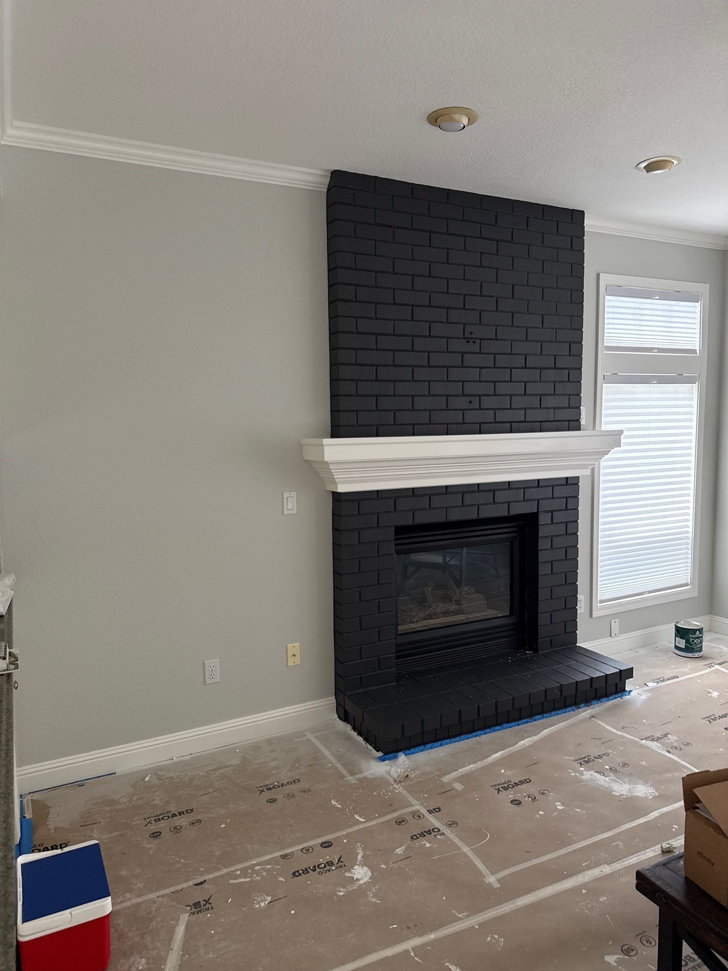 Living room with black brick fireplace, white mantel, gray walls, and construction debris on the floor