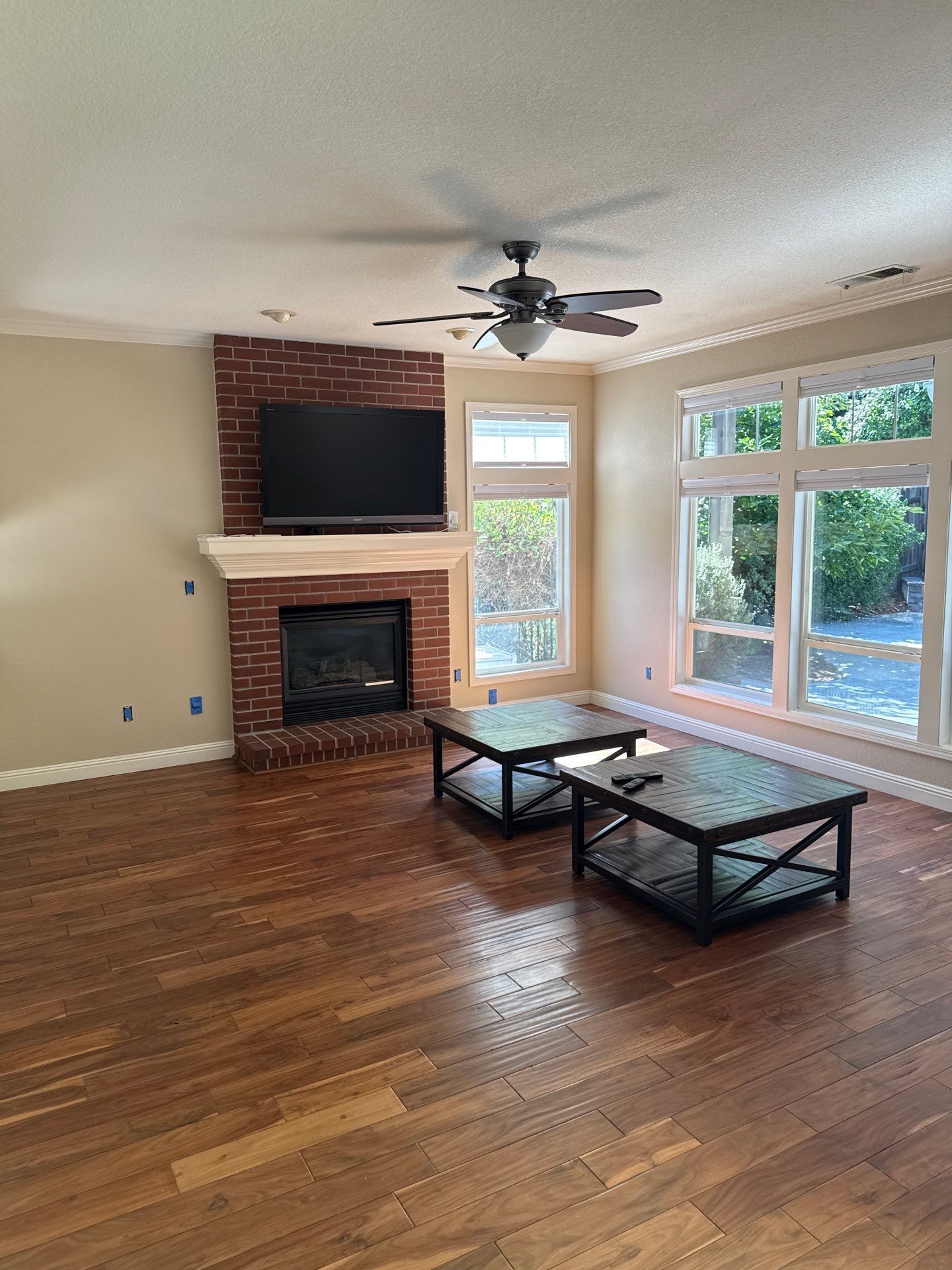 Spacious living room with fireplace, TV, ceiling fan, hardwood floors, and large windows.