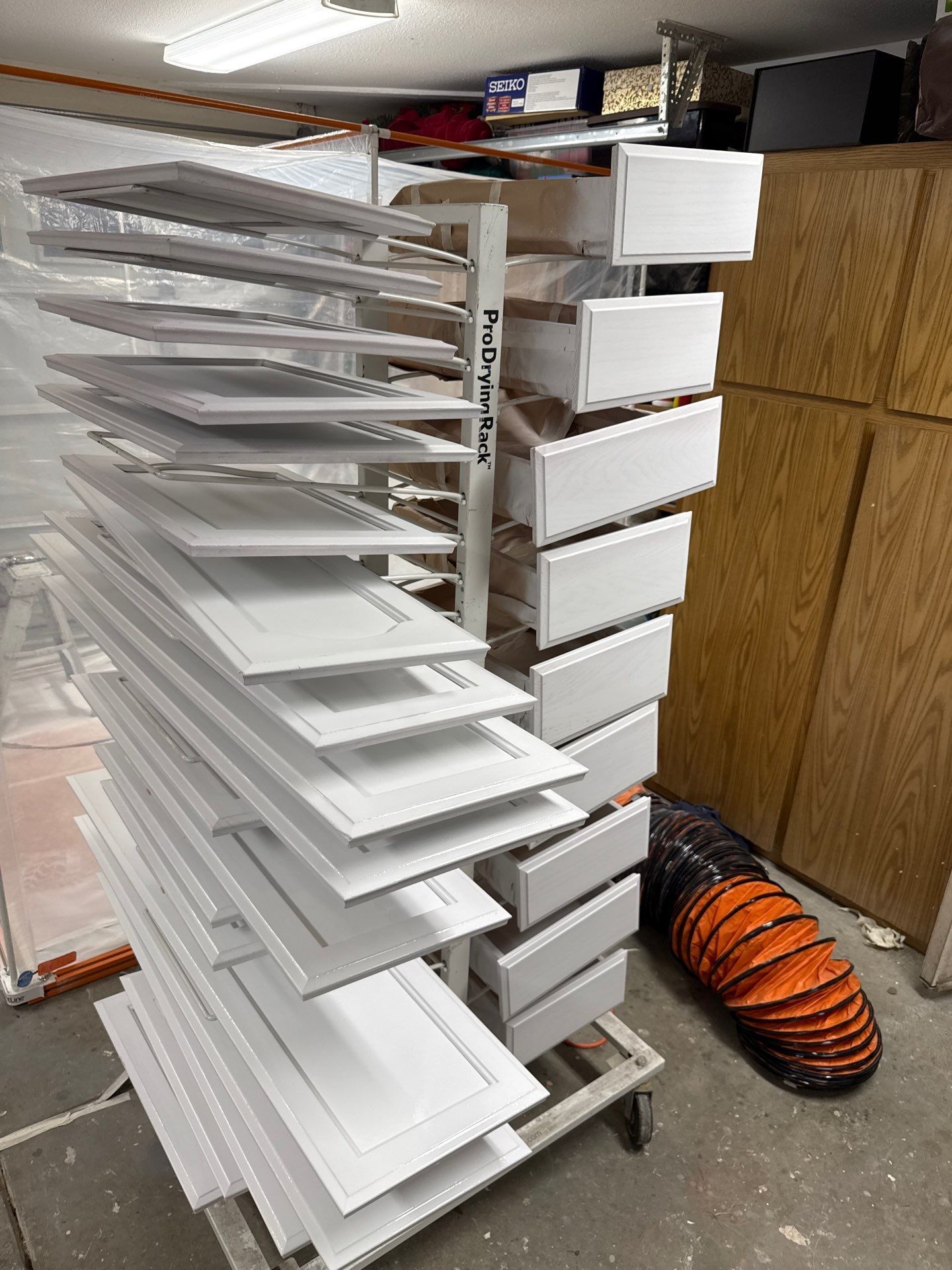 Metal storage rack with stacked white trays and boxes in a workshop, next to an orange hose