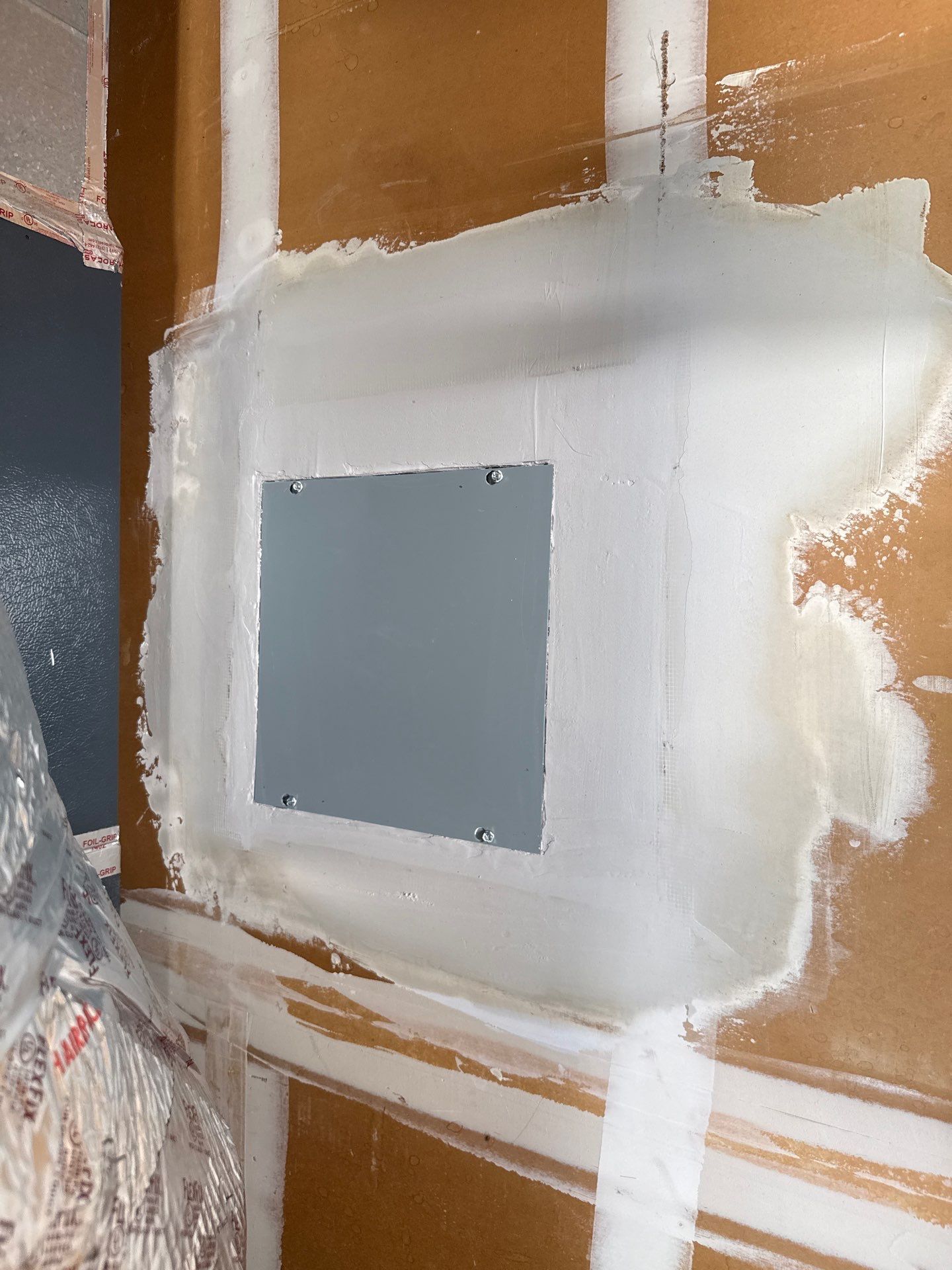 White drywall patch with a gray square inset on a brown wall under renovation