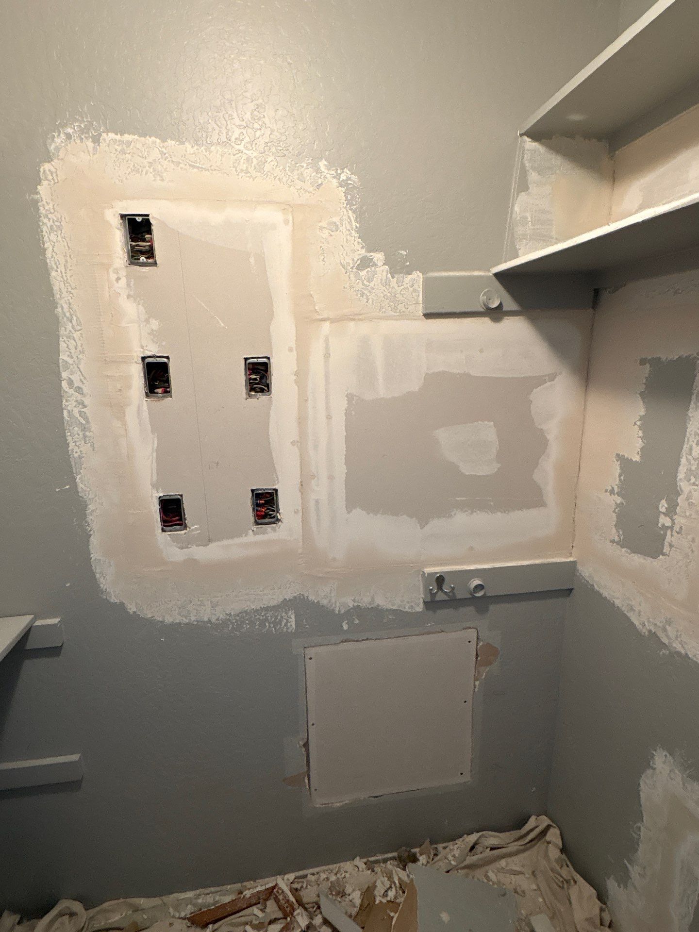 Unfinished utility closet with patched drywall, electrical box openings, and gray and white primer on the walls.