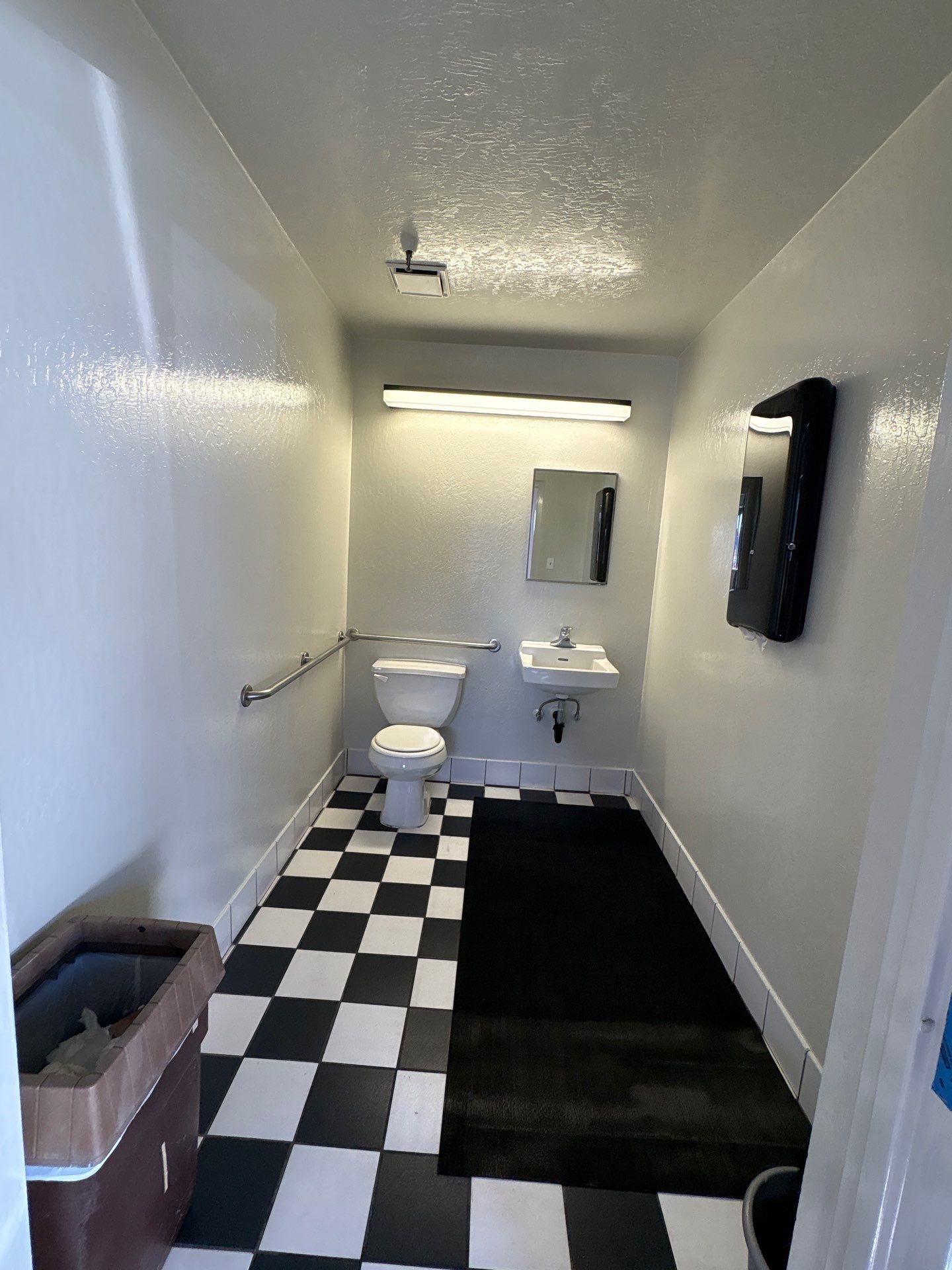 Small bathroom with black-and-white tile floor, toilet, sink, mirror, and wall-mounted TV.