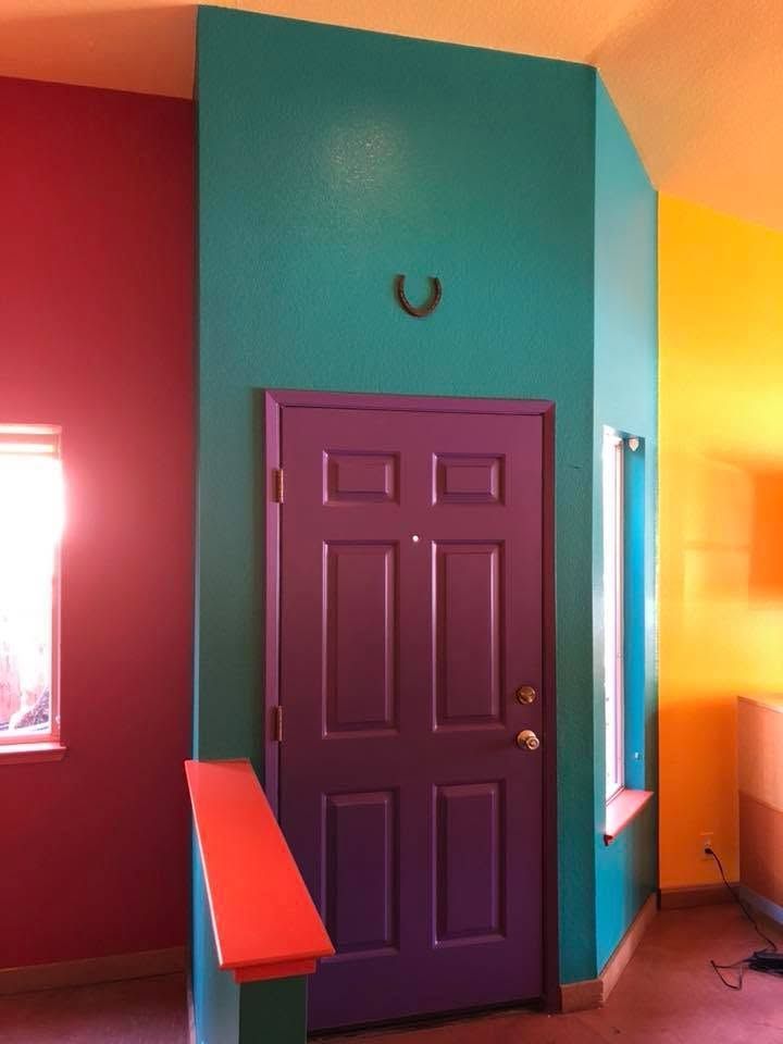 Colorful interior with a purple door on a teal wall, bright red and yellow walls, and a small window.
