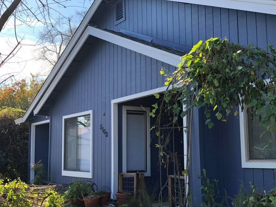 Blue house exterior with white trim, front entrance, and leafy vines by the doorway