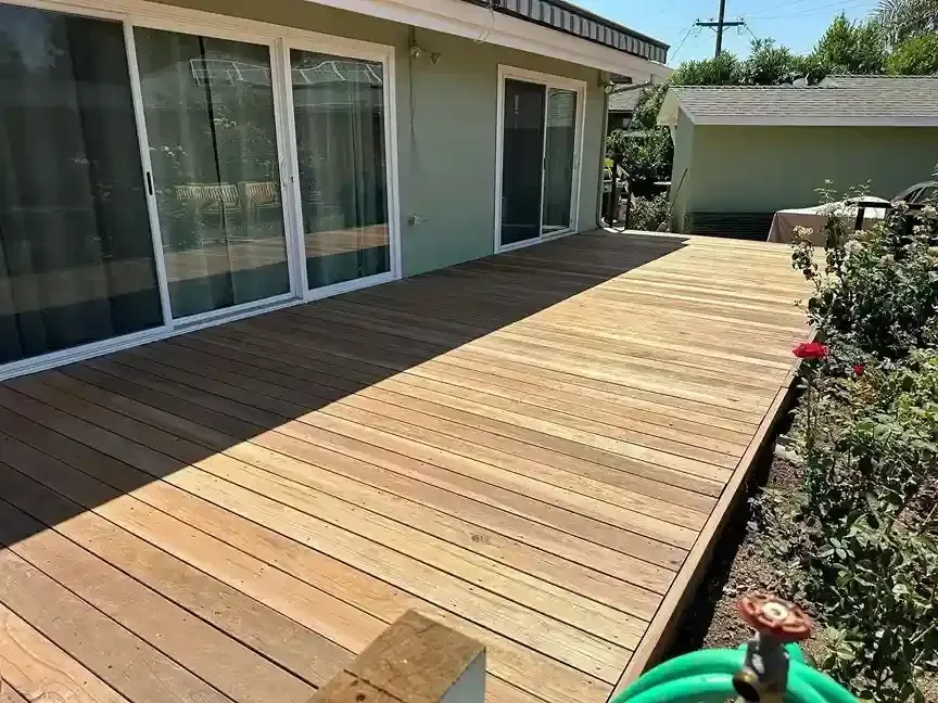 Wooden deck beside a house with sliding glass doors and potted flowers in sunlight