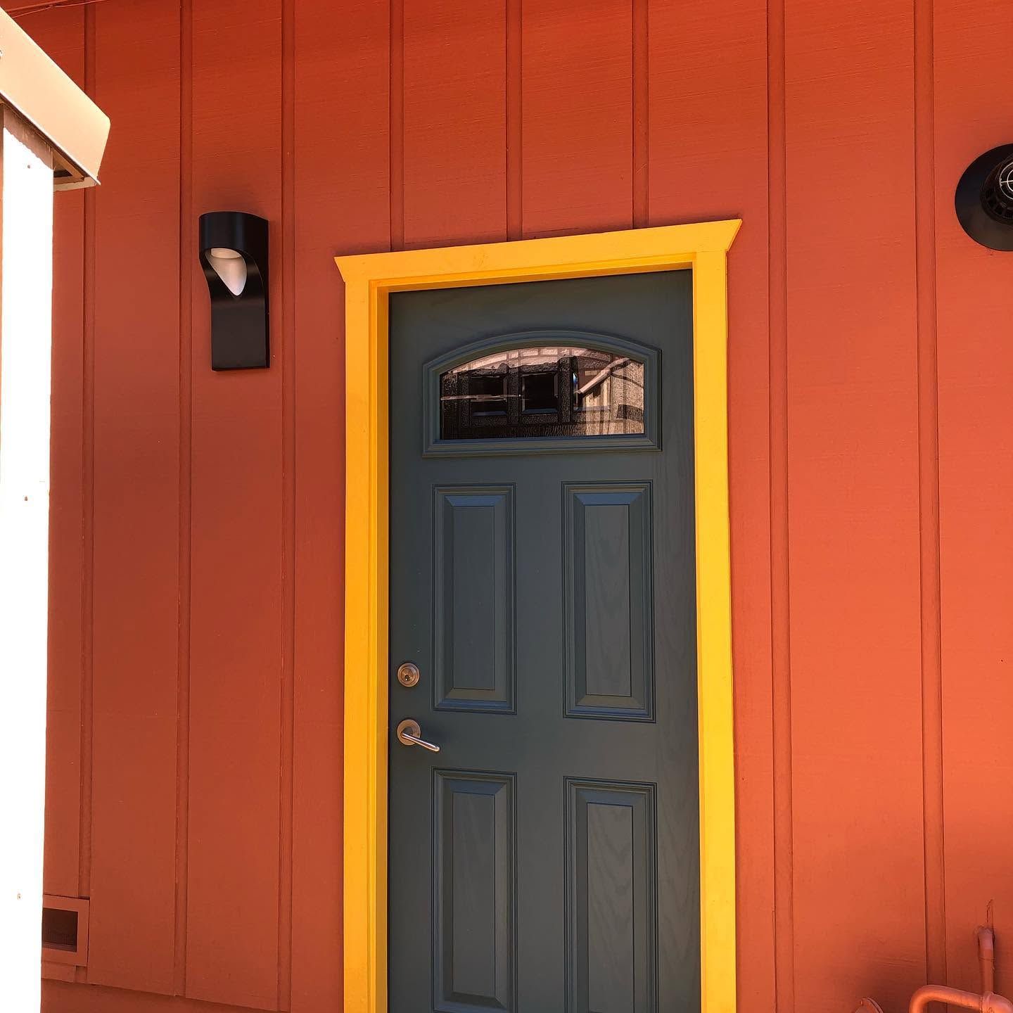 Gray door with yellow trim on an orange exterior wall, with a wall-mounted light beside it