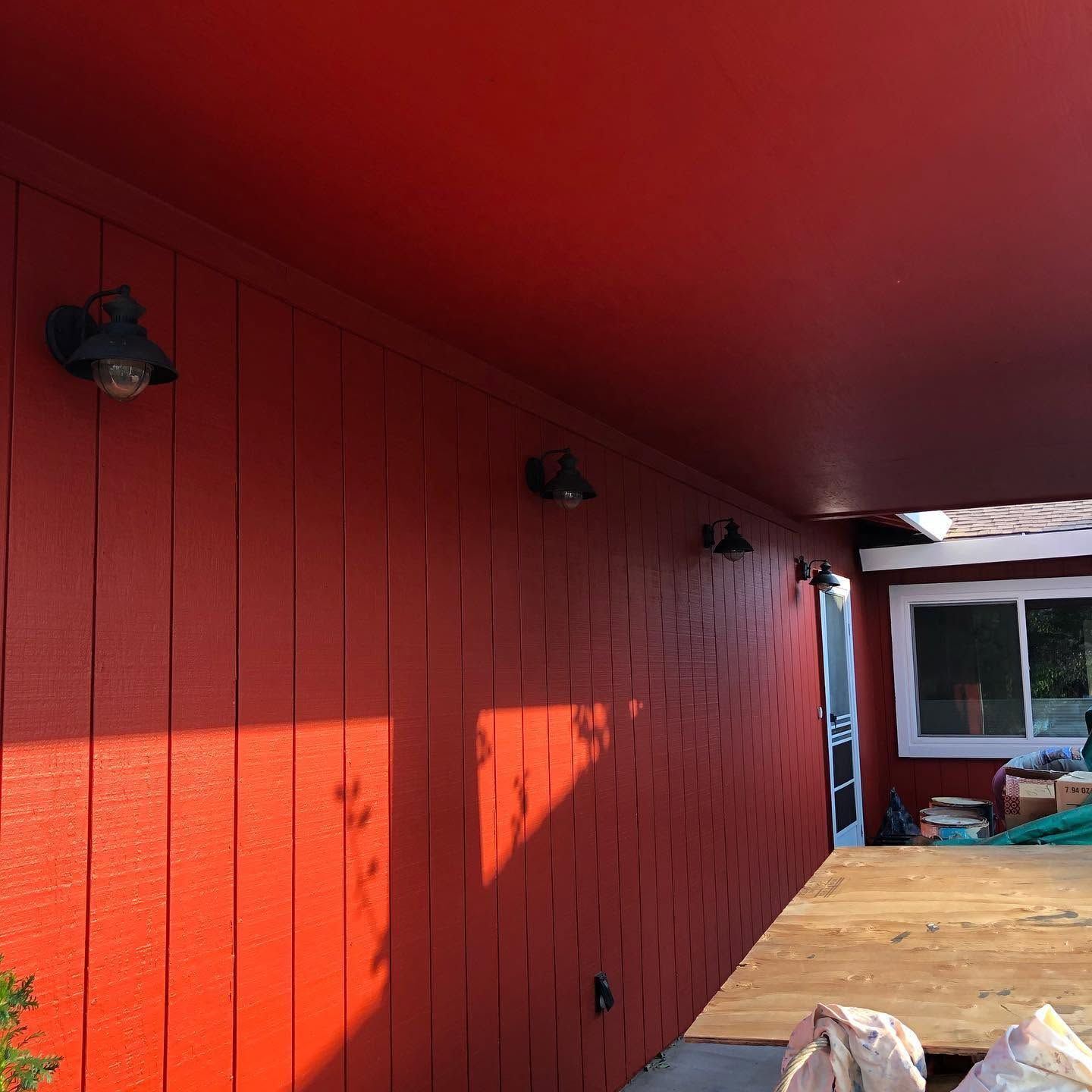 Red-painted exterior wall and ceiling of a covered patio with black lights and a wooden deck area.
