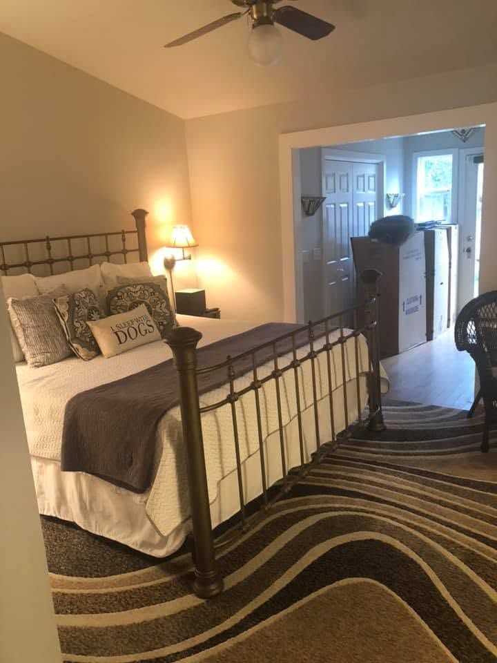 Bedroom with iron bed, nightstand lamp, patterned rug, and open doorway to a bathroom.