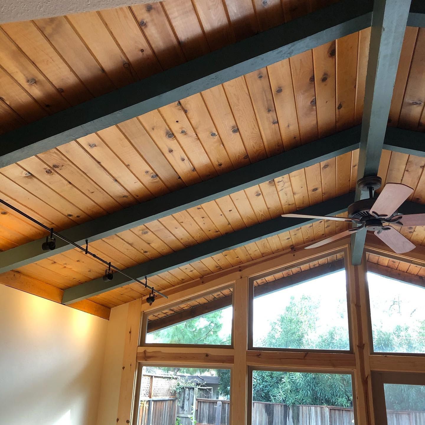 Wooden vaulted ceiling with exposed beams, skylight windows, and a ceiling fan in a bright room