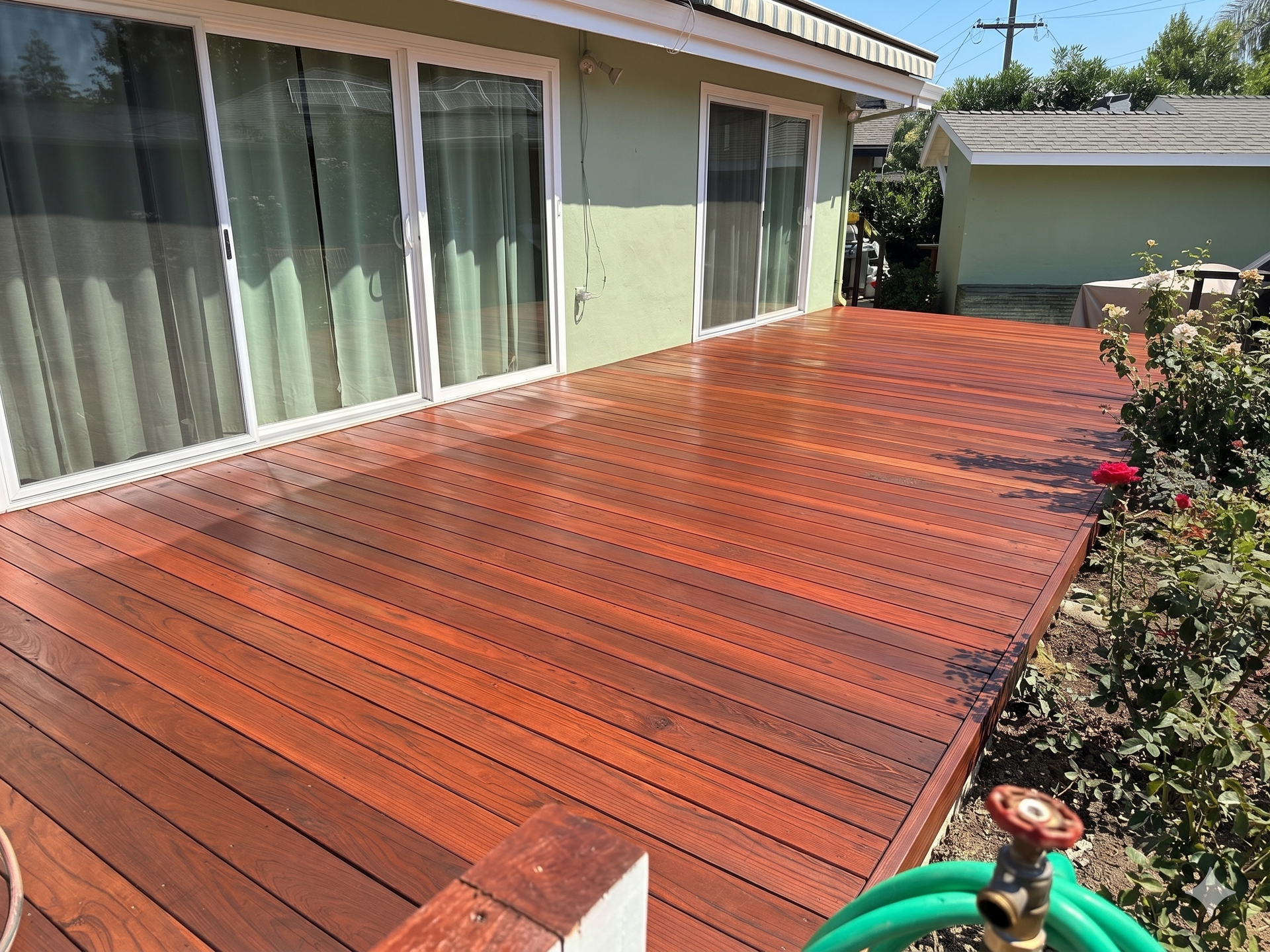Wooden deck beside a house with sliding glass doors and a small garden border