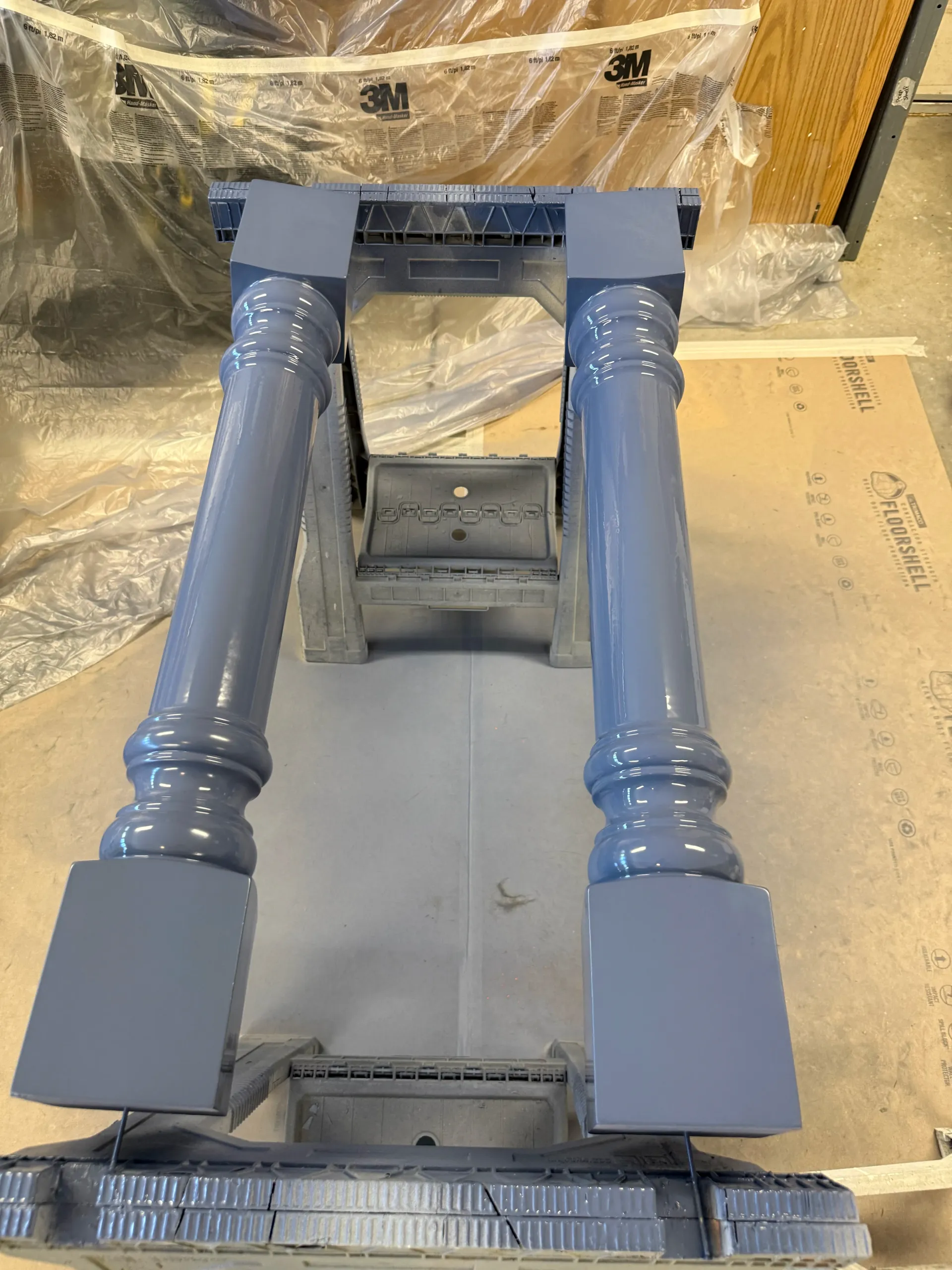 Blue decorative rail balusters on a protected floor, part of an indoor construction or renovation site