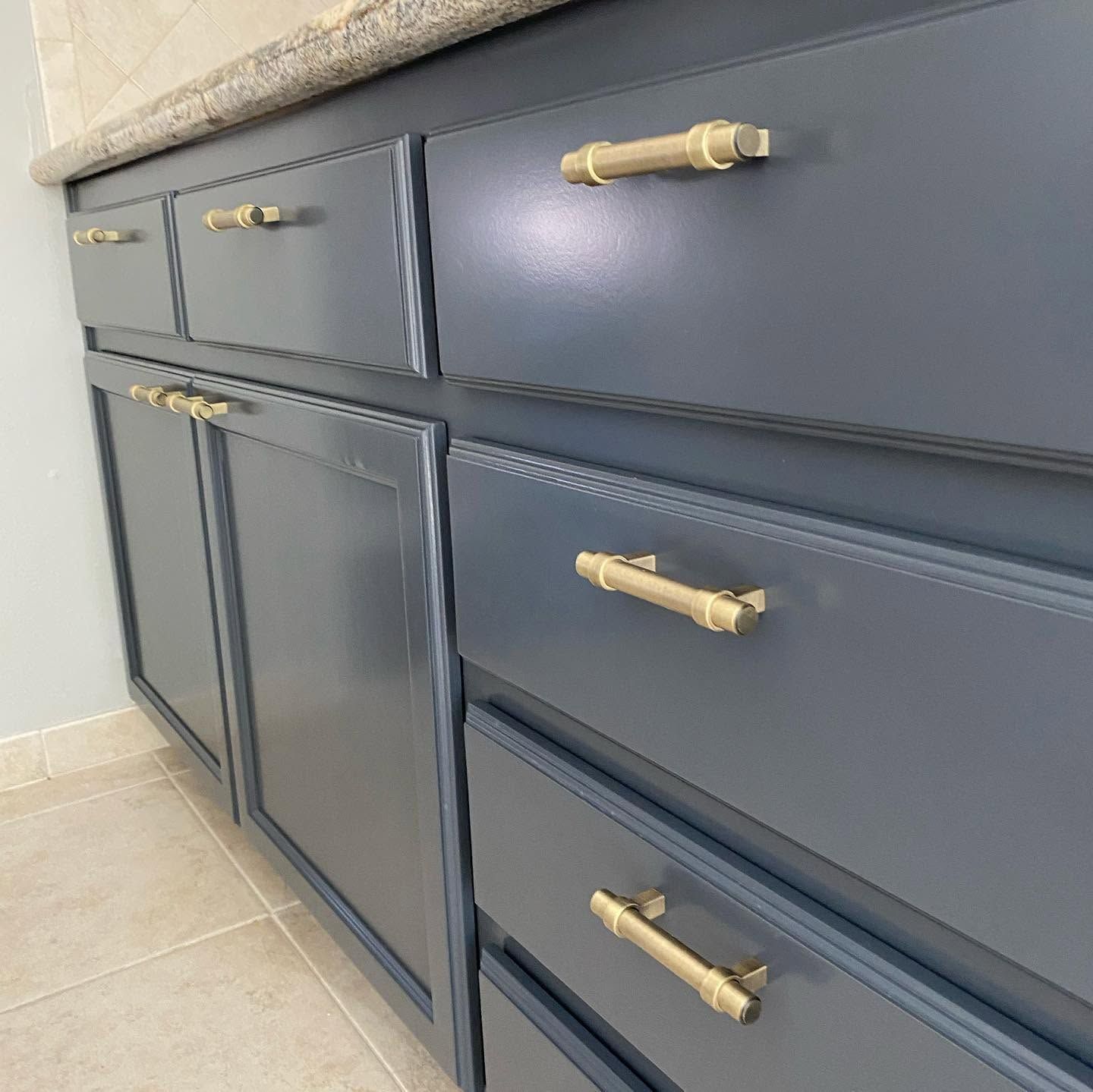 Slate blue kitchen cabinets with brass handles and a light stone countertop, viewed at an angle
