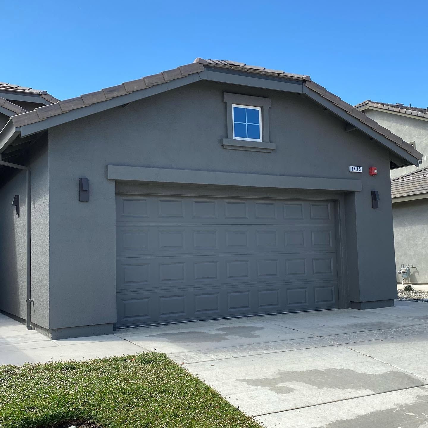 Gray single-story house with a two-car garage and small front lawn under a clear blue sky