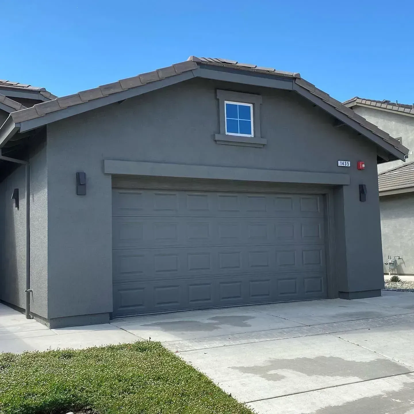 Gray single-story house with a two-car garage and small front lawn under a clear blue sky