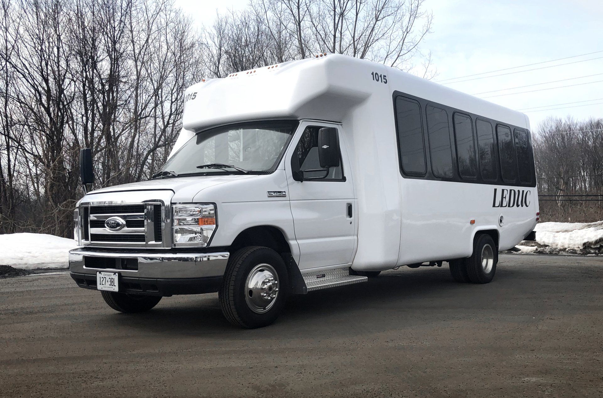 White shuttle bus parked on a snowy roadside with leafless trees in the background