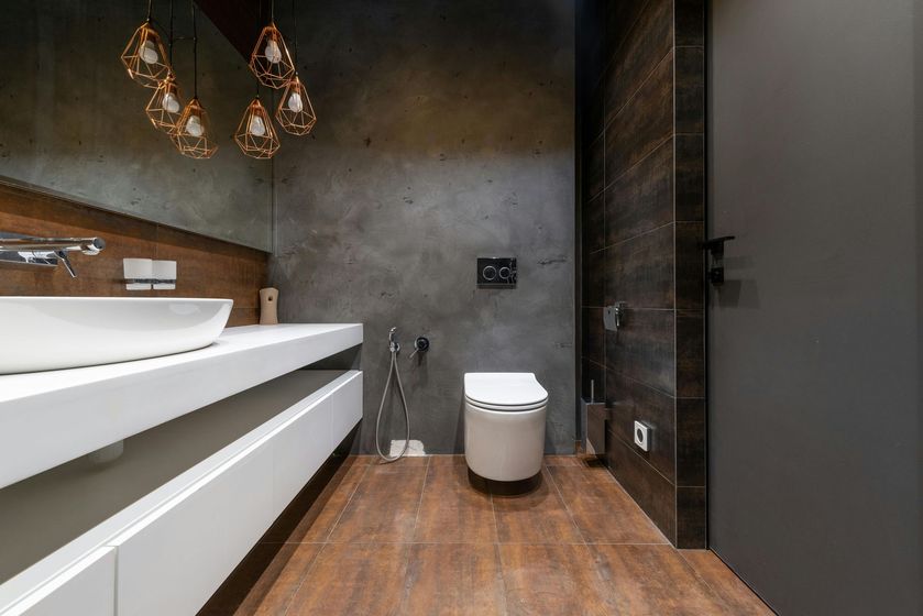 Modern bathroom with a white bathtub, wall-mounted toilet, dark walls, and wood flooring