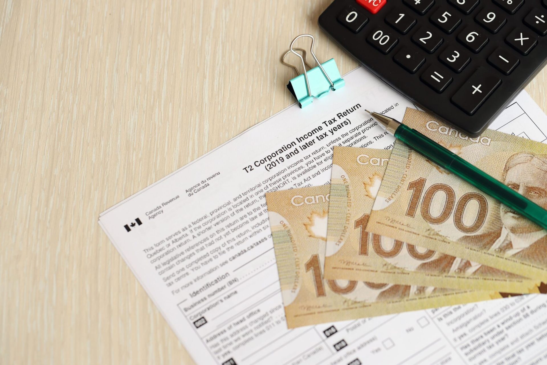 Canadian tax form, calculator, pencil, and Canadian $100 bills on a wooden surface.