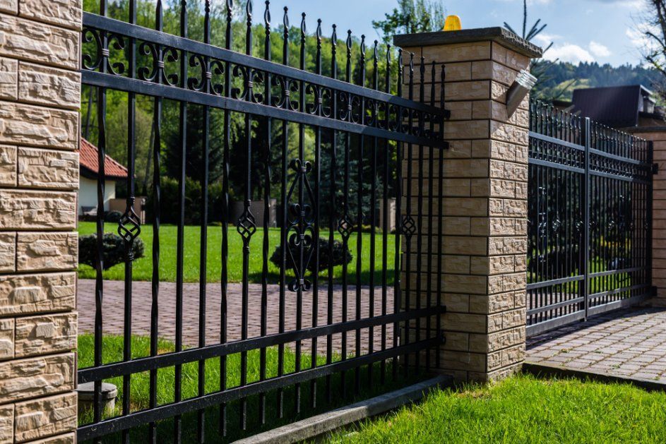 A Black Wrought Iron Fence Surrounds a Brick Wall and A Driveway — Coastline Glass Pool Fencing in Smiths Lake, NSW