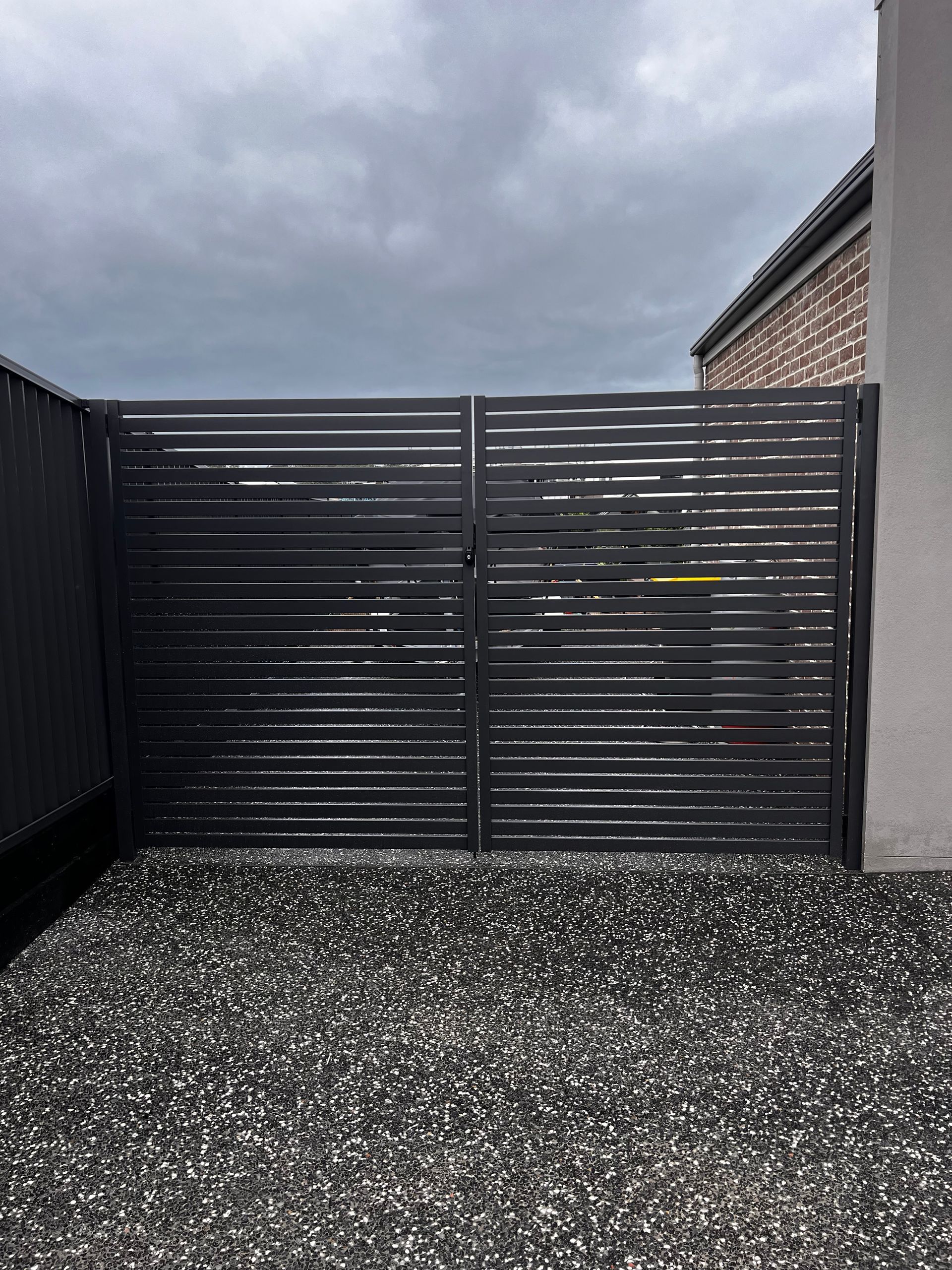 A Black Gate Is Sitting on Top of A Gravel Driveway — Coastline Glass Pool Fencing in Old Bar, NSW