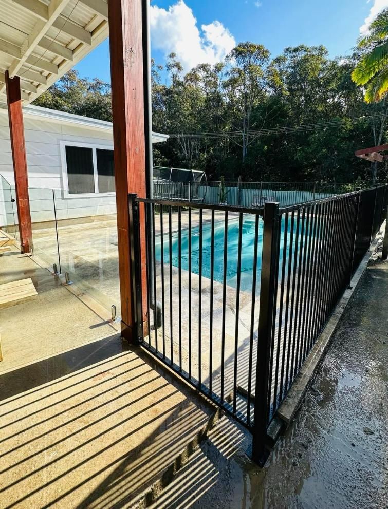 A Black Metal Safety Fence Secures a Swimming Pool on A Patio — Coastline Glass Pool Fencing in Old Bar, NSW
