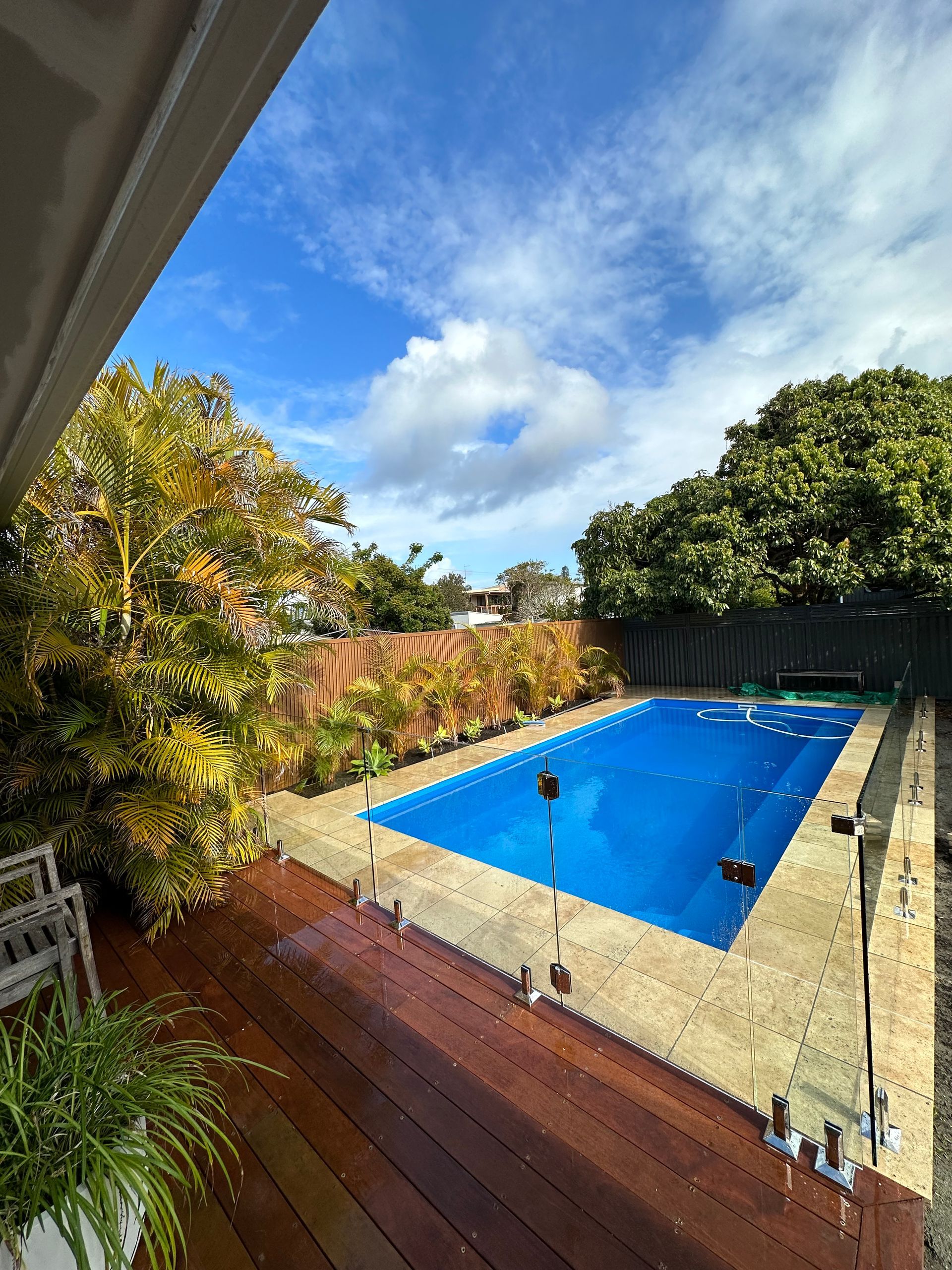 A Large Swimming Pool Is Surrounded by Trees and A Wooden Deck — Coastline Glass Pool Fencing in Old Bar, NSW