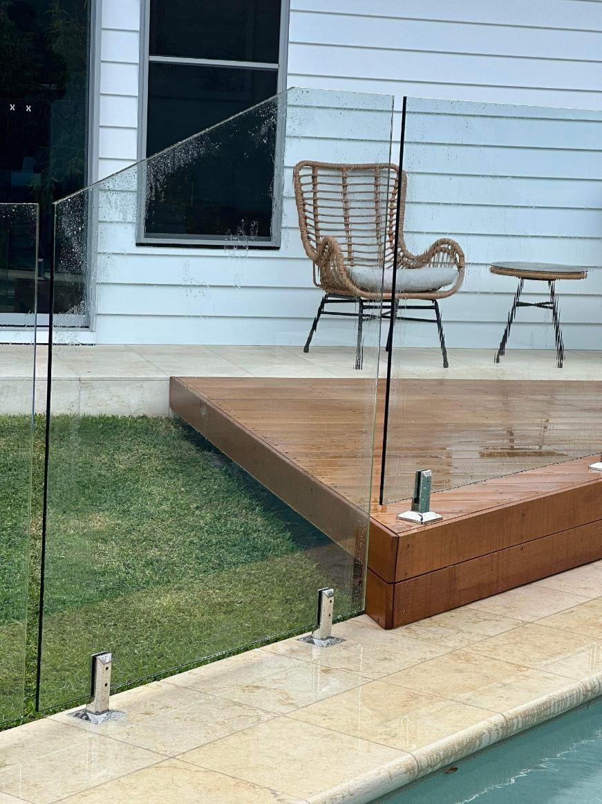 A Glass Pool Fence Sits Between a Patio with A Wicker Chair and Table — Coastline Glass Pool Fencing in Old Bar, NSW