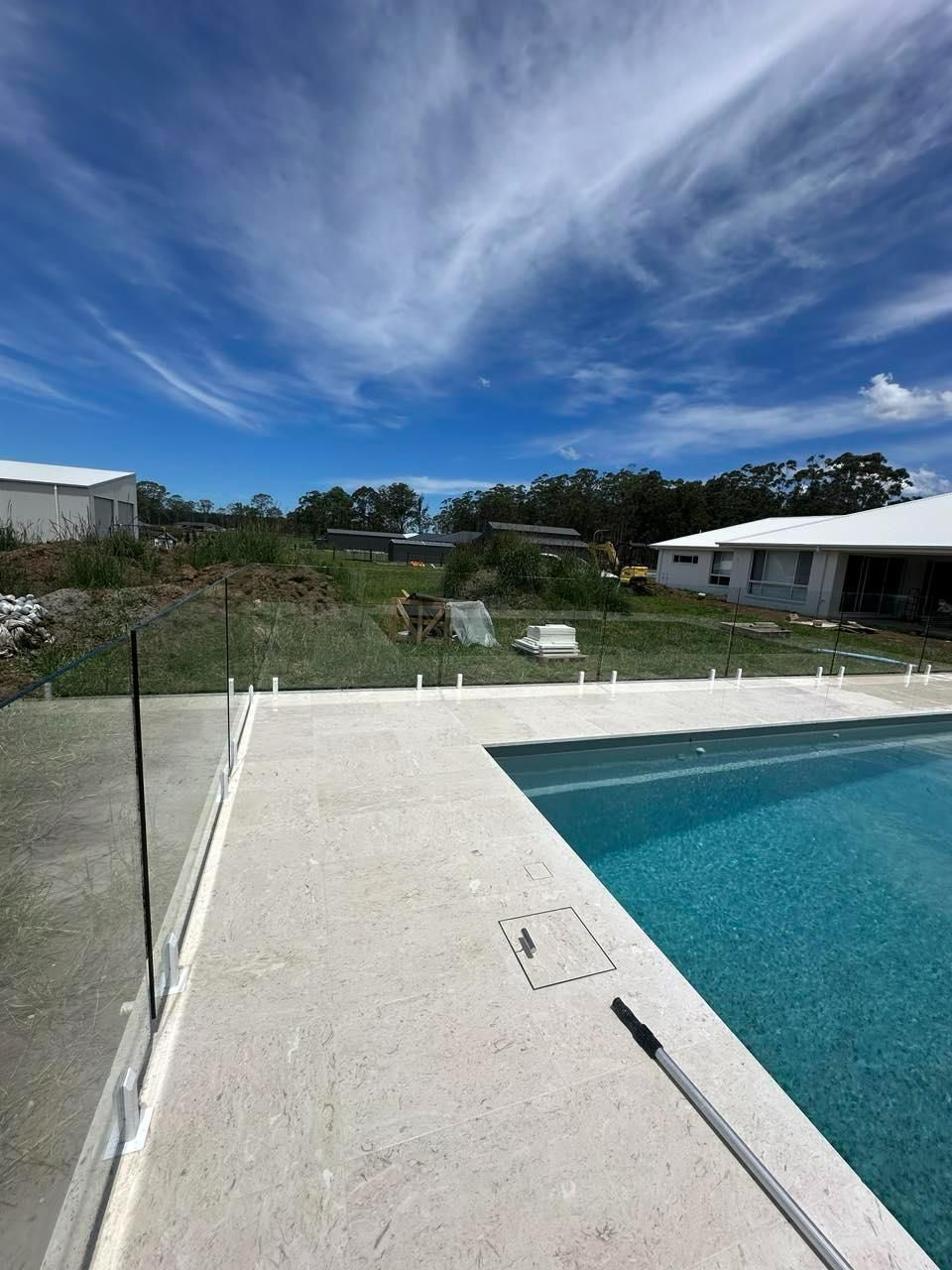 A Swimming Pool with A White House in The Background — Coastline Glass Pool Fencing in Old Bar, NSW