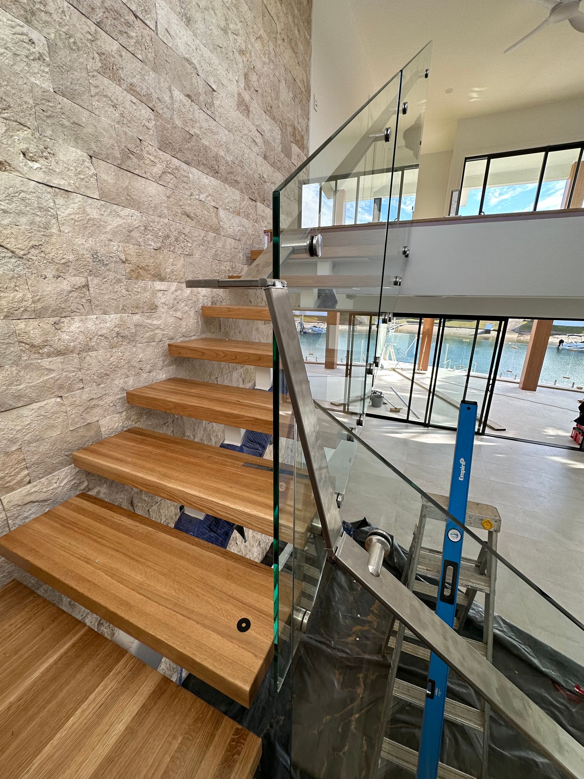 Floating Wooden Staircase with A Glass Railing and Stone Feature Wall — Coastline Glass Pool Fencing in Old Bar, NSW