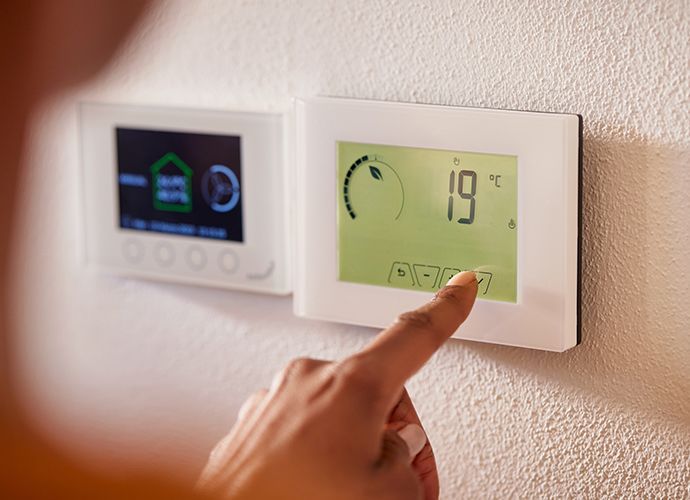 Une personne appuie sur un bouton d'un thermostat mural affichant une température de 19 degrés Celsius.