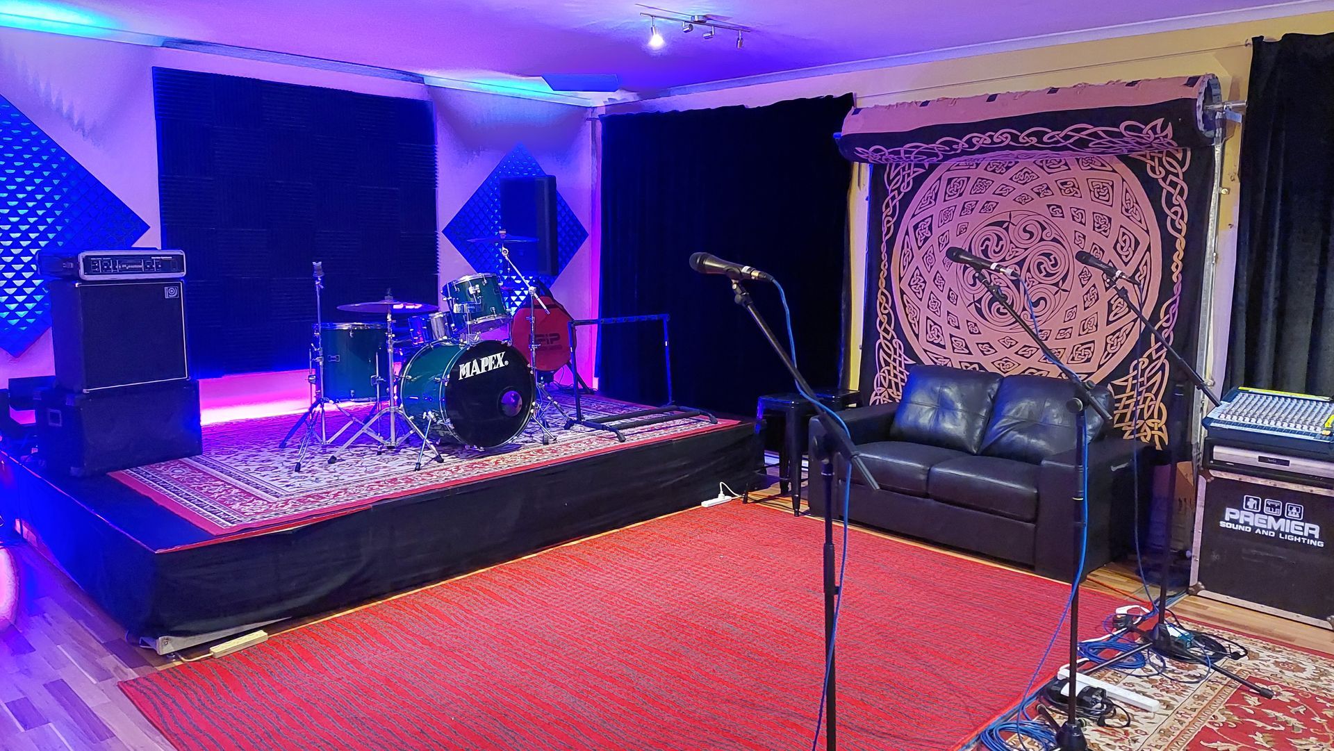 A room with a couch and a microphone and a drum set on a stage.