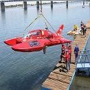Red rescue helicopter hovering above a dock beside a body of water, with people nearby.