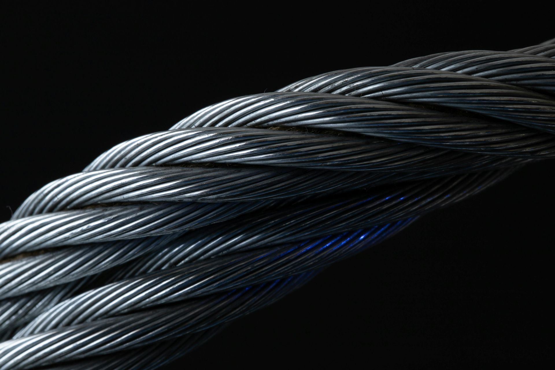 Close-up of intertwined steel cables with blue highlights on a black background
