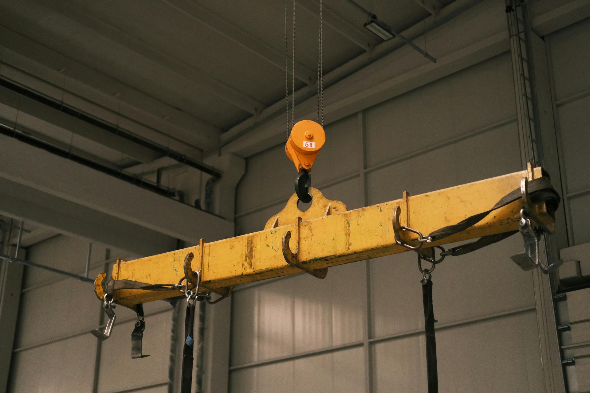 Yellow industrial crane beam suspended indoors by an orange hoist hook.