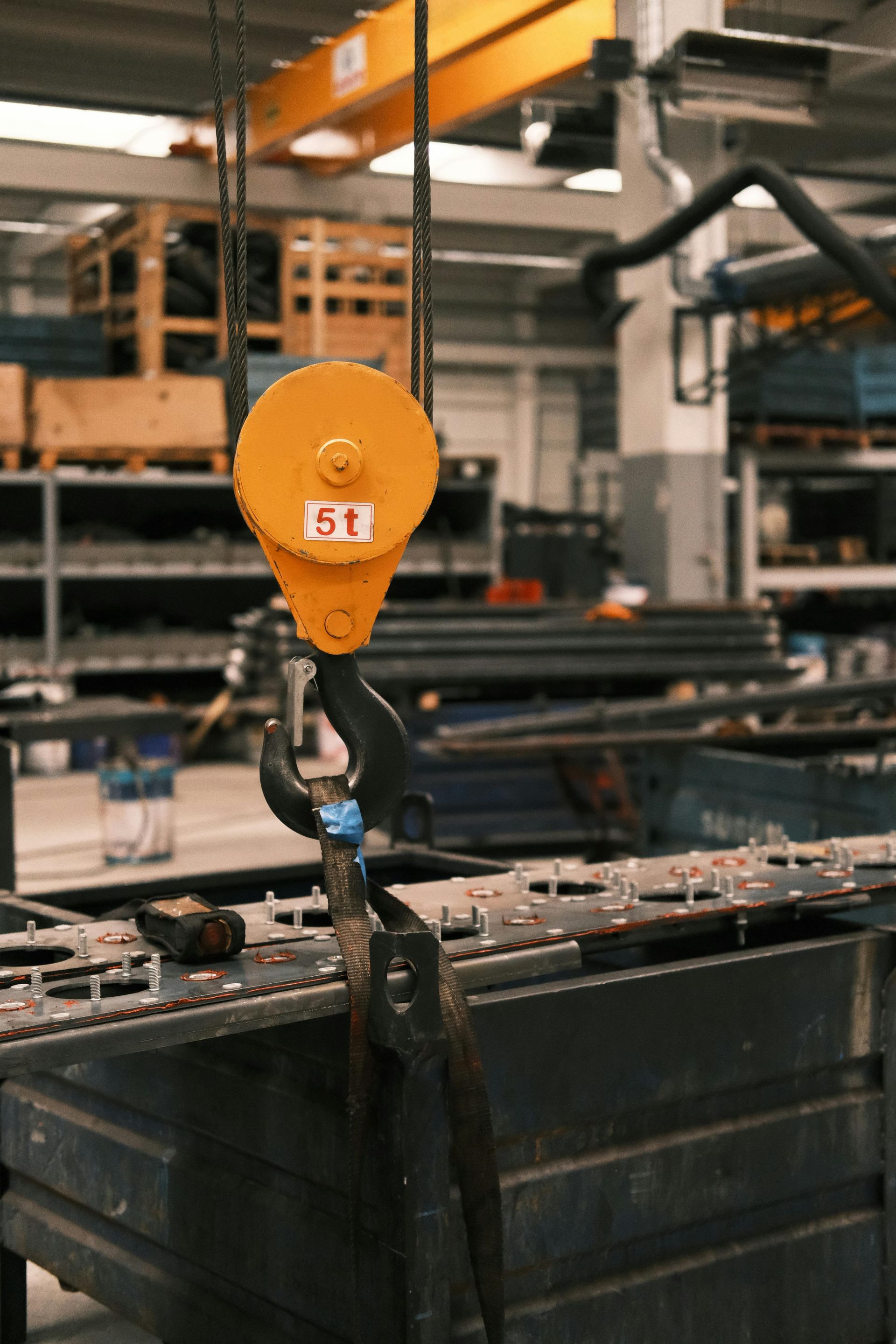 Orange industrial crane hook lifting a black metal container in a warehouse