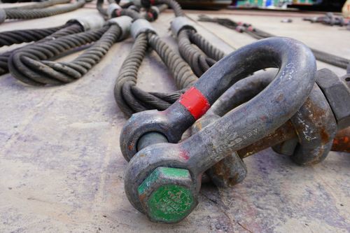Coiled heavy-duty chains and a metal shackle on a dusty work surface, marked with red and green paint.