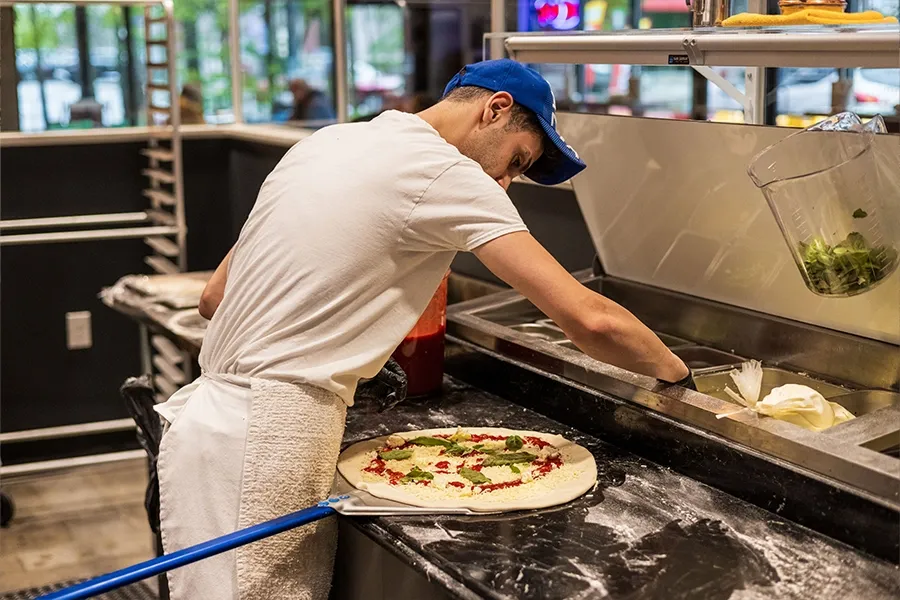 Chef stretching pizza dough in a commercial kitchen with toppings nearby