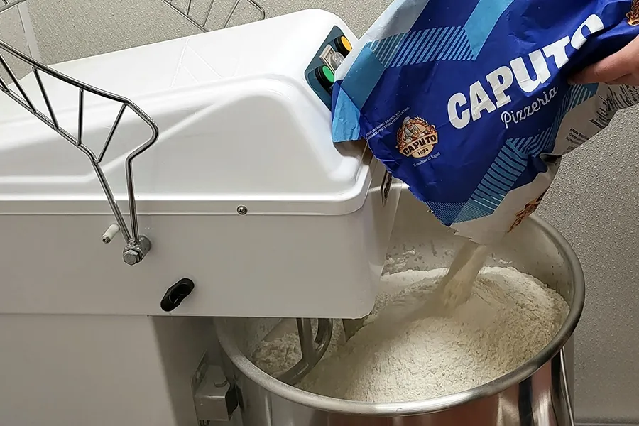 White machine dispensing grain from a blue bag into a metal bowl